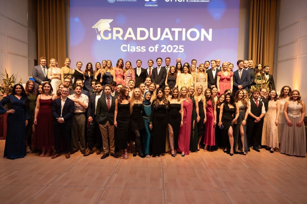 Gruppenfoto einer Abschlussfeier mit zahlreichen Absolventinnen und Absolventen auf einer Bühne vor einer Projektionswand mit der Aufschrift „GRADUATION Class of 2025“.